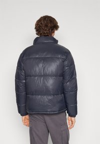 Marineblauwe pufferjas met een hoge kraag, doorgestikt ontwerp en een glanzende textuur. Voorzien van een lichtgewicht constructie en elastische manchetten.