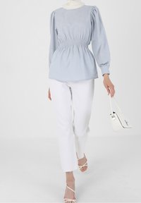 Vaaleansininen puffihihainen paita, jossa on rypytetty vyötärö, yhdistetty valkoisiin suoriin housuihin ja remmikorkokenkiin. Valkoinen käsilaukku viimeistelee asun.