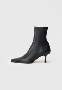 Botas de cuero negras hasta el tobillo con puntera afilada y caña ajustada. El tacón es bajo y en bloque, con una textura suave y un diseño minimalista.