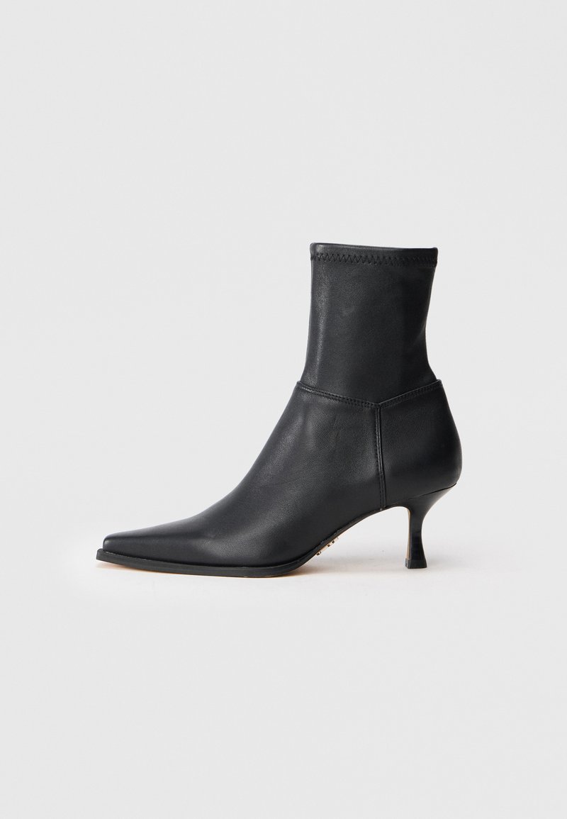 Botas de cuero negras hasta el tobillo con puntera afilada y caña ajustada. El tacón es bajo y en bloque, con una textura suave y un diseño minimalista.