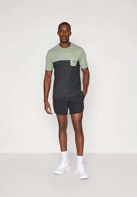 Heren T-shirt in lichtgroen en marineblauw, met een borstzakje en logodetail. Gecombineerd met zwarte shorts en witte sneakers.