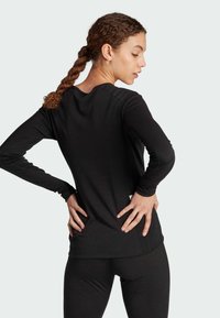Maglia nera a maniche lunghe con scollatura rotonda, design aderente e texture morbida. La vista posteriore mostra i dettagli delle cuciture e una piccola etichetta all'orlo.