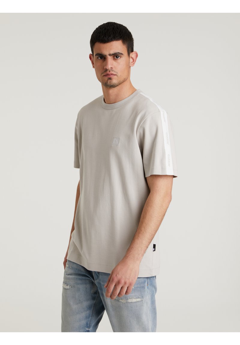 T-shirt grigio chiaro a maniche corte realizzato in cotone, con colletto rotondo e un piccolo logo sul petto. Strisce bianche sui fianchi delle maniche.
