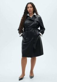 Schwarzer Leder-Trenchcoat mit doppelt geknöpften Knöpfen, tailliertem Gürtel und Seitentaschen; verfügt über einen klassischen Kragen und weiße Hemdmanschetten.