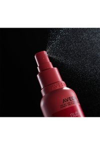 Bouteille pulvérisateur rouge avec une buse large et texturée ; un brouillard d'eau se dispersant depuis le haut sur un fond noir. Étiquette "AVEDA" visible.