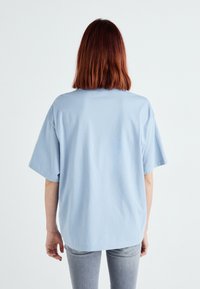 Lysblå oversized bomulds T-shirt med korte ærmer, rund halsudskæring og en afslappet pasform, der har en glat tekstur og ingen synlige grafikker.