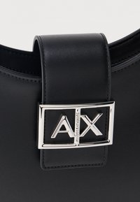 Μαύρο κούμπωμα από δερμάτινη τσάντα με ασημένια ορθογώνια αγκράφα που διαθέτει ανάγλυφα γράμματα "A|X" και ραμμένες λεπτομέρειες.