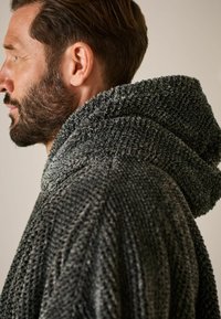 Grauer Kapuzenumhang aus strukturiertem Stoff, mit einer dicken, weichen Kapuze und lockerer Passform, seitlich betrachtet, wobei die Weichheit des Materials hervorgehoben wird.