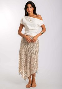 Haut blanc à épaules dénudées et jupe beige ornée de sequins argentés dans un motif diagonal. Des sandales à lanières complètent le look.