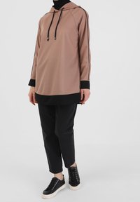 Sudadera con capucha y mangas largas en suave tela beige con acentos negros. Presenta un dobladillo y puños negros, combinada con jeans negros y zapatillas con cordones.