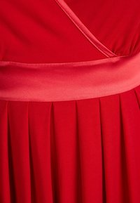 Röd klänning med en slät textur, med ett brett satinskärp och en veckad kjol för extra volym och rörelse.