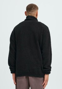 Schwarze Fleecejacke mit hohem Kragen, lockerer Passform und strukturiertem Stoff. Verfügt über lange Ärmel und einen geraden Saum ohne sichtbare Beschläge.
