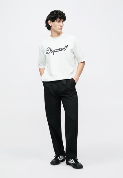White t-shirt with black "Dsquared²" logo, paired with black trousers and black shoes featuring white stripes. Set against a plain background.