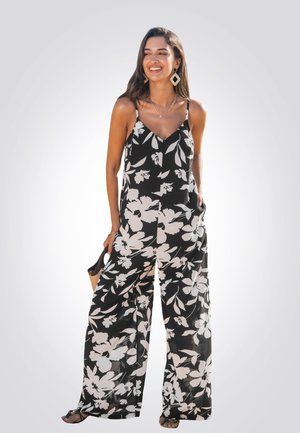 Black floral jumpsuit with wide legs, thin straps, and a v-neckline, featuring large white flower patterns and a loose, flowing design.