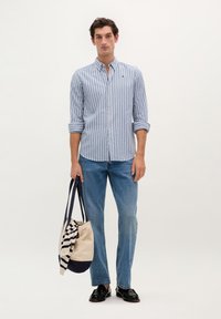 Stribet skjorte i blå og hvid, parret med lyseblå jeans. Holder en cremet og marineblå tote taske med stribede detaljer.