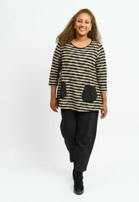 Stribet top i beige og sort med trekvartærmer og to sorte lommer, parret med sorte brede bukser og ankelstøvler.