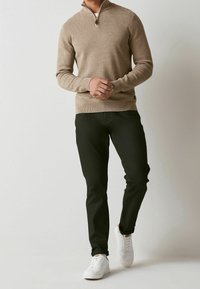Beige zip-up sweater with a textured finish, paired with fitted black trousers and white sneakers. Sweater features a stand collar detail.