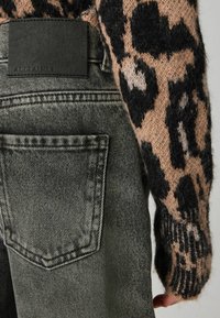 Suéter ligero con un patrón de leopardo en beige y negro, combinado con jeans de mezclilla gris que cuentan con un bolsillo trasero y una etiqueta de cuero de la marca.