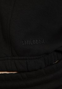 Los pantalones de chándal negros cuentan con una textura suave, una cinturilla elástica y un sutil logotipo "SMILODOX" bordado.