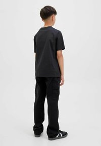 Zwarte katoenen T-shirt met korte mouwen, gecombineerd met zwarte cargobroek met zijzakken en een ontspannen pasvorm, gedragen met zwarte sneakers.