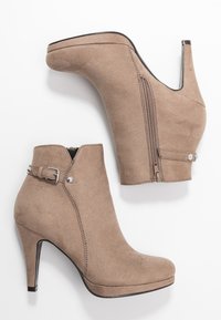 Botas de tobillo de imitación ante beige con tacón alto, cremallera lateral y un detalle de hebilla. Presentan una textura suave y un diseño de puntera redonda.