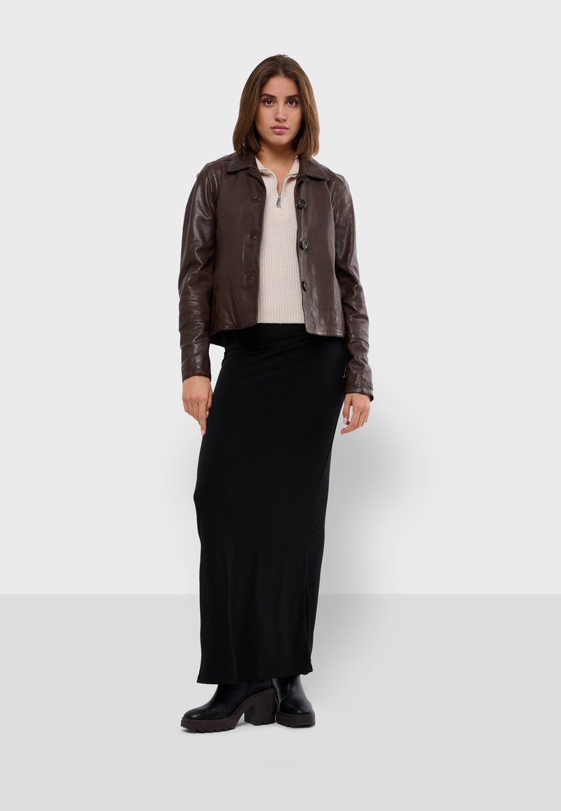 Brązowa skórzana kurtka z kołnierzem i guzikami z przodu, noszona na kremowym swetrze. Na dole długa czarna spódnica i czarne buty na obcasie.