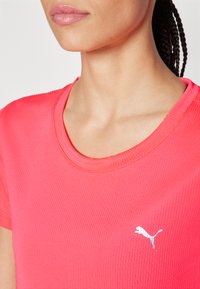 Rosa ribbet idretts T-skjorte med rund hals og korte ermer. Har en liten hvit Puma-logo på venstre bryst.