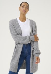 Graham gestrickter Cardigan mit gerippten Bündchen und Saum, offenem Vorderteil und einem strukturierten Muster, kombiniert mit einem weißen T-Shirt und blauen Jeans.