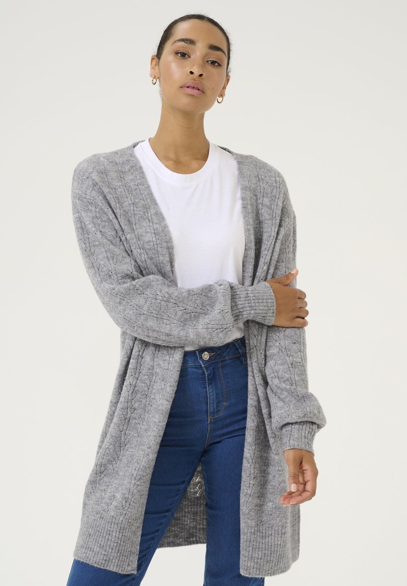 Graham gestrickter Cardigan mit gerippten Bündchen und Saum, offenem Vorderteil und einem strukturierten Muster, kombiniert mit einem weißen T-Shirt und blauen Jeans.