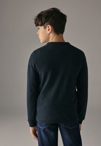 Mörkblå topp med långa ärmar i mjukt tyg. Har rund halsringning och ribbade muddar, kombinerad med mörkblå jeans. Enkel design.