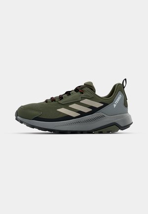 Scarpa sportiva verde con tomaia in rete, dettagli grigi, tre strisce grigie chiare, suola nera e lacci rossi. Presenta un tallone a strappo.