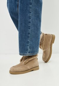 Tansuede enkellaarsjes met bontafwerking, platte zool en ronde neus. Draag met omgeslagen blauwe spijkerbroek, wat een casual stijl laat zien.