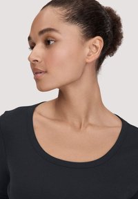 Zwarte top met een ronde hals en een zachte textuur, met korte mouwen. Het profiel van het model benadrukt een gedefinieerde kaaklijn en een natuurlijke huidtint.