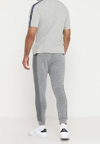 Grijze sport T-shirt met korte mouwen en marineblauwe logo-accents, gecombineerd met grijze joggers met taps toelopende pijpen en contrasterende zijkanten.
