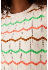 Gebreid topje met een crème basis en zigzagpatronen in bruin, groen, oranje en roze. Fijn textiel met verticale strepen.