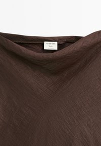 Brun tekstureret stof med en ujævn overflade; fastgjort etiket læser "Massimo Dutti Studio, Fremstillet i Portugal."