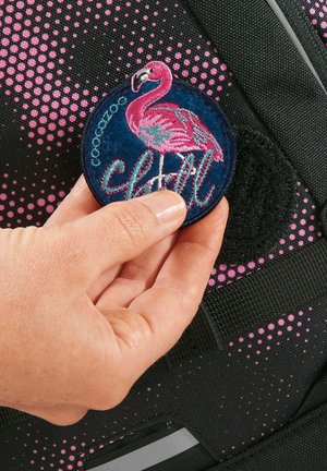 Patch rond brodé présentant un flamant rose et le mot "chill", attaché à un sac à dos noir à motifs de points roses.