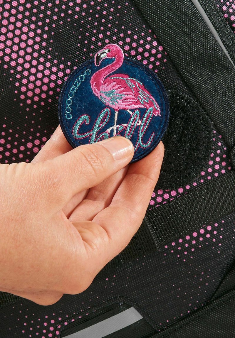 Runder gestickter Patch mit einem rosa Flamingo und dem Wort "chill", befestigt an einem schwarzen Rucksack mit rosa Punktmustern.