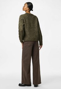 Oliivroheline kootud sviiter tekstuuri mustri ja koonusdetailidega, kombineeritud laia säärega pruunide pükstega ja mustade kingadega.