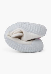 Zapatillas slip-on de lona blanca con suela de goma texturizada, con puntera redondeada y plantilla acolchada, dobladas ordenadamente hacia adentro.