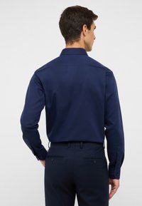 Donkerblauwe overhemd met lange mouwen, een gestructureerde kraag, textuurstof en knoopmanchetten. Tailored fit met achterpand yoke details.
