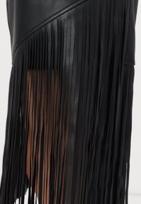 Fekete bőrszoknya, amely hosszú, lelógó rojtokkal díszített az egyik oldalon, sima tapintással és aszimmetrikus dizájnnal.