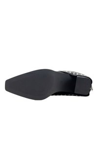 Zapato de cuero negro con una suela de goma texturizada; presenta tachuelas plateadas a lo largo de la parte superior y un cierre de cremallera lateral.