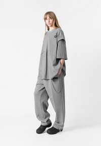 Camiseta gris de gran tamaño con mangas cortas y cuello redondo, combinada con pantalones grises holgados que cuentan con bolsillos laterales y un detalle de cadena.