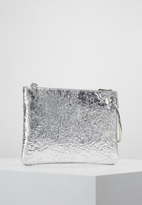 Silverfärgad metalclutch med en krinklad textur, stängd med ett blixtlås, och med ett silvrigt ringhandtag på ena sidan.