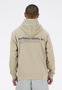 Béžová mikina s kapucí a volným střihem, na zádech velké logo a nápis. Měkká látka, dlouhé rukávy a žebrované manžety.