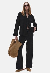 Set composto da camicia in tessuto nero stropicciato e pantaloni a gamba larga, abbinato a una borsa intrecciata color nocciola e mule maculati marroni, con maniche lunghe e una vestibilità rilassata.