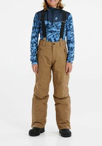 Hnedé snehové nohavice s nastaviteľnými čiernymi ramienkami, nosené cez dlhý rukáv modrého vzorovaného trička. Čierne snehové čižmy dotvárajú outfit.
