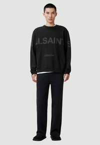 Sweatshirt preto com impressões "ALLSAINTS" e "LONDRINA", gola redonda, punhos e barra canelados. Combinado com calças escuras e sapatos slip-on.