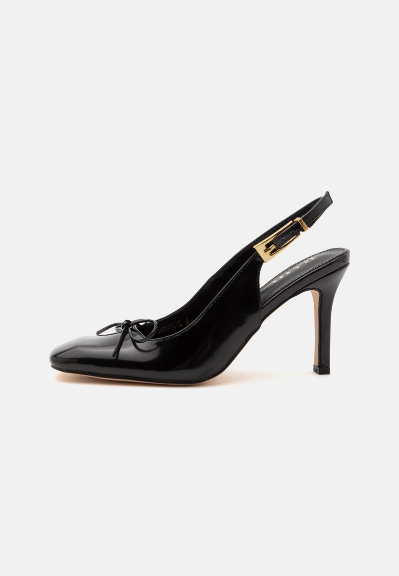 Chaussure slingback à talon haut en cuir verni noir, bout pointu, petit nœud sur le devant et bride à boucle dorée sur fond clair.